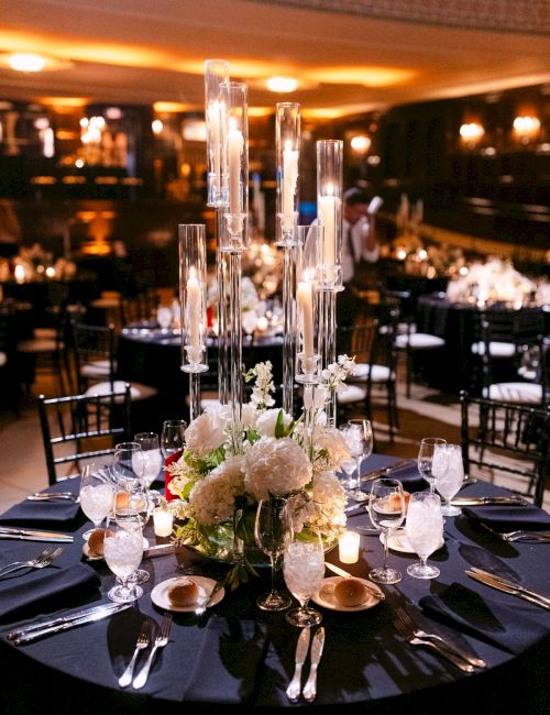 A beautifully set table with flowers, candles, glassware, and silverware in a dimly lit, elegant event space.