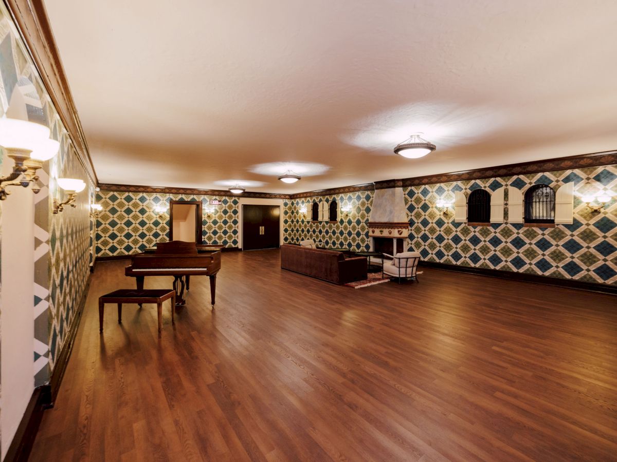 A spacious room with patterned walls, wooden flooring, a piano, and seating areas under soft lighting, creating a warm atmosphere.